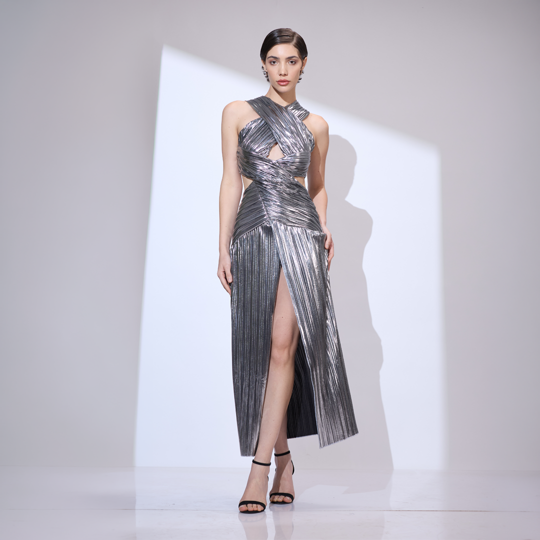 Image of A shimmering Haute Couture metallic silver gown with a pleated texture, featuring a dramatic crossover halter neckline, waist cut-outs, and a high center-leg slit.