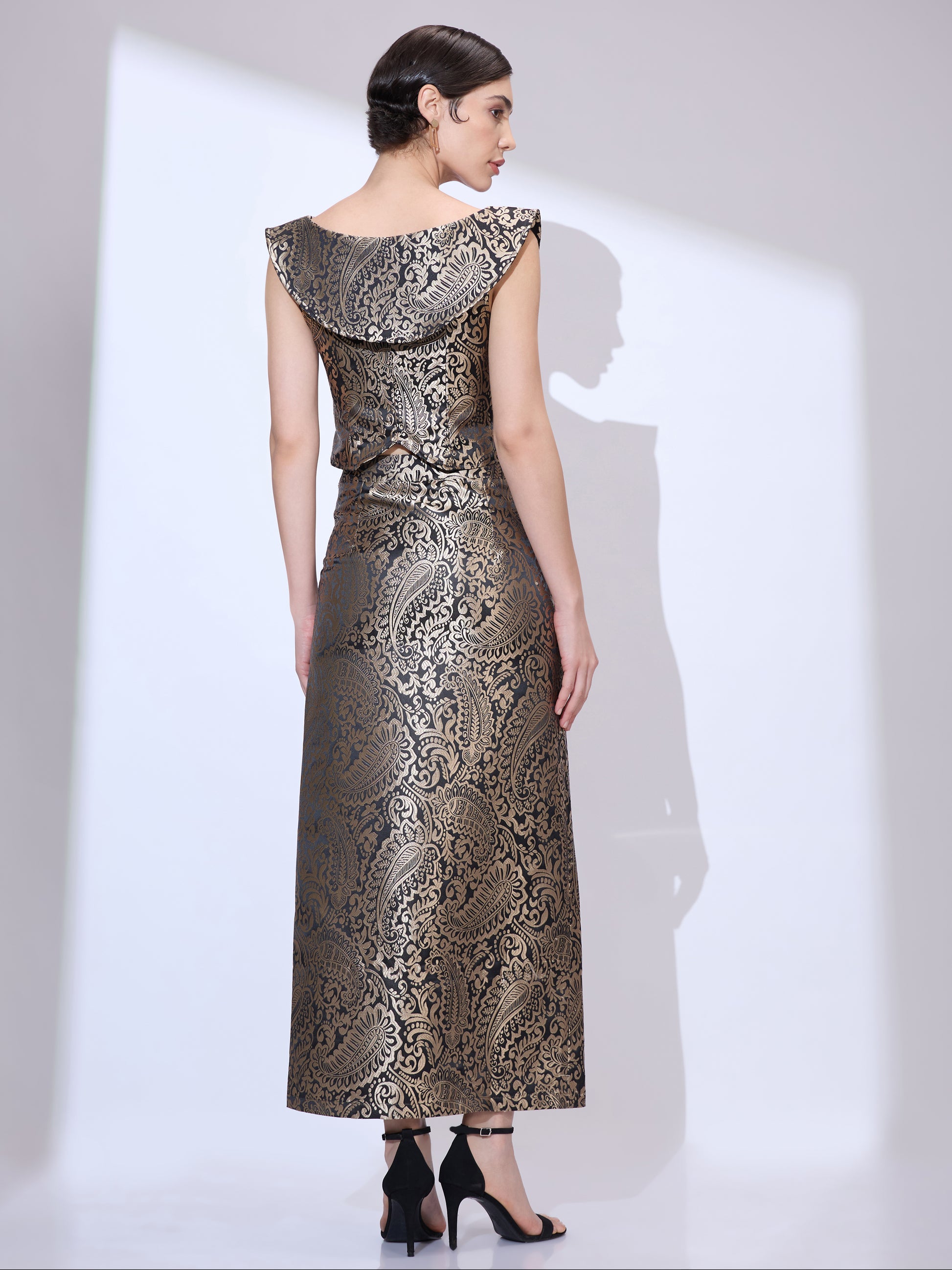 Back view of woman wearing a black and gold metallic paisley formal co ord with cropped top and floor-length pencil skirt