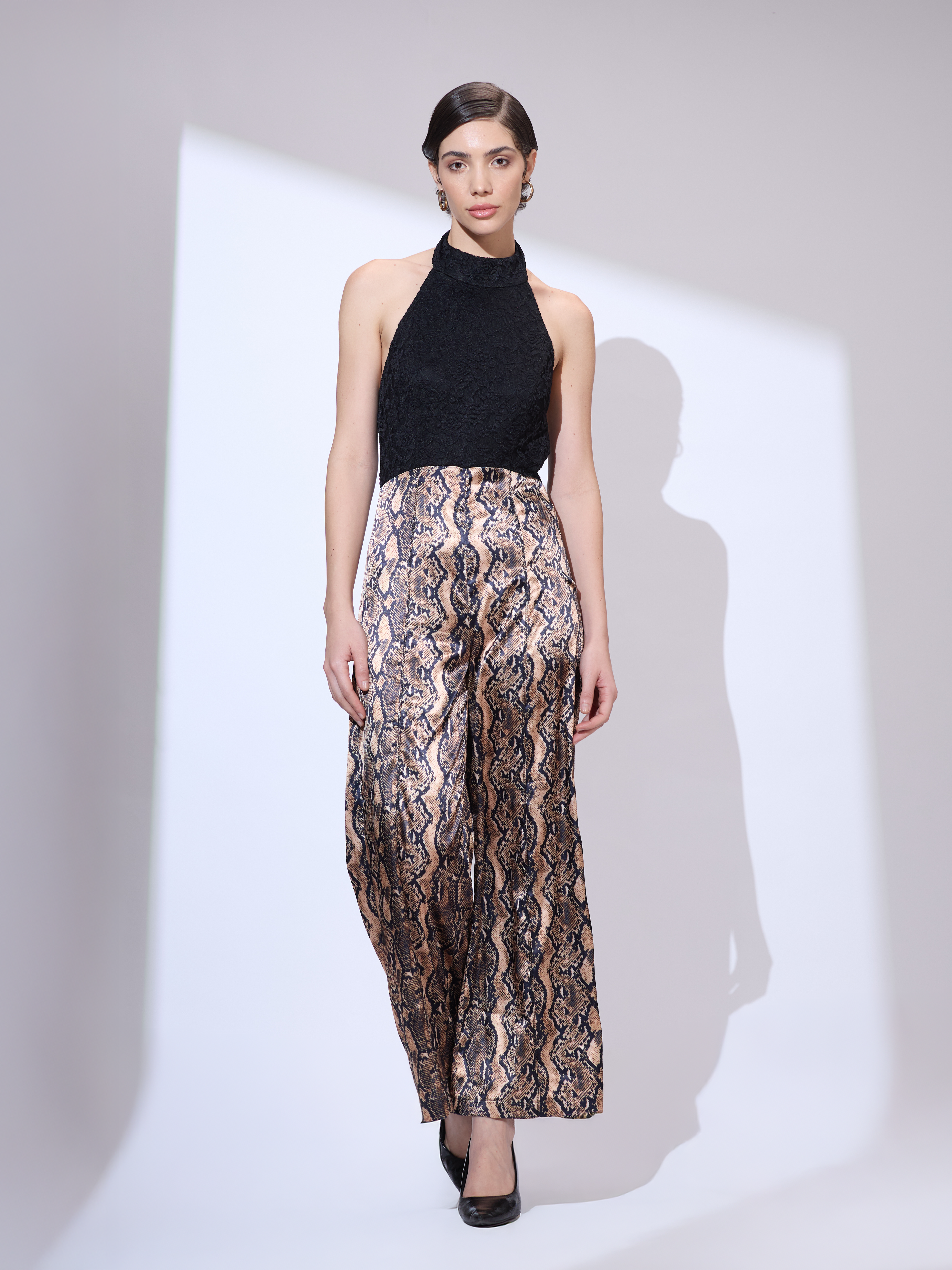 Image of Standing straight in a black and gold metallic snakeskin halter neck jumpsuit with an elegant wide-leg silhouette.