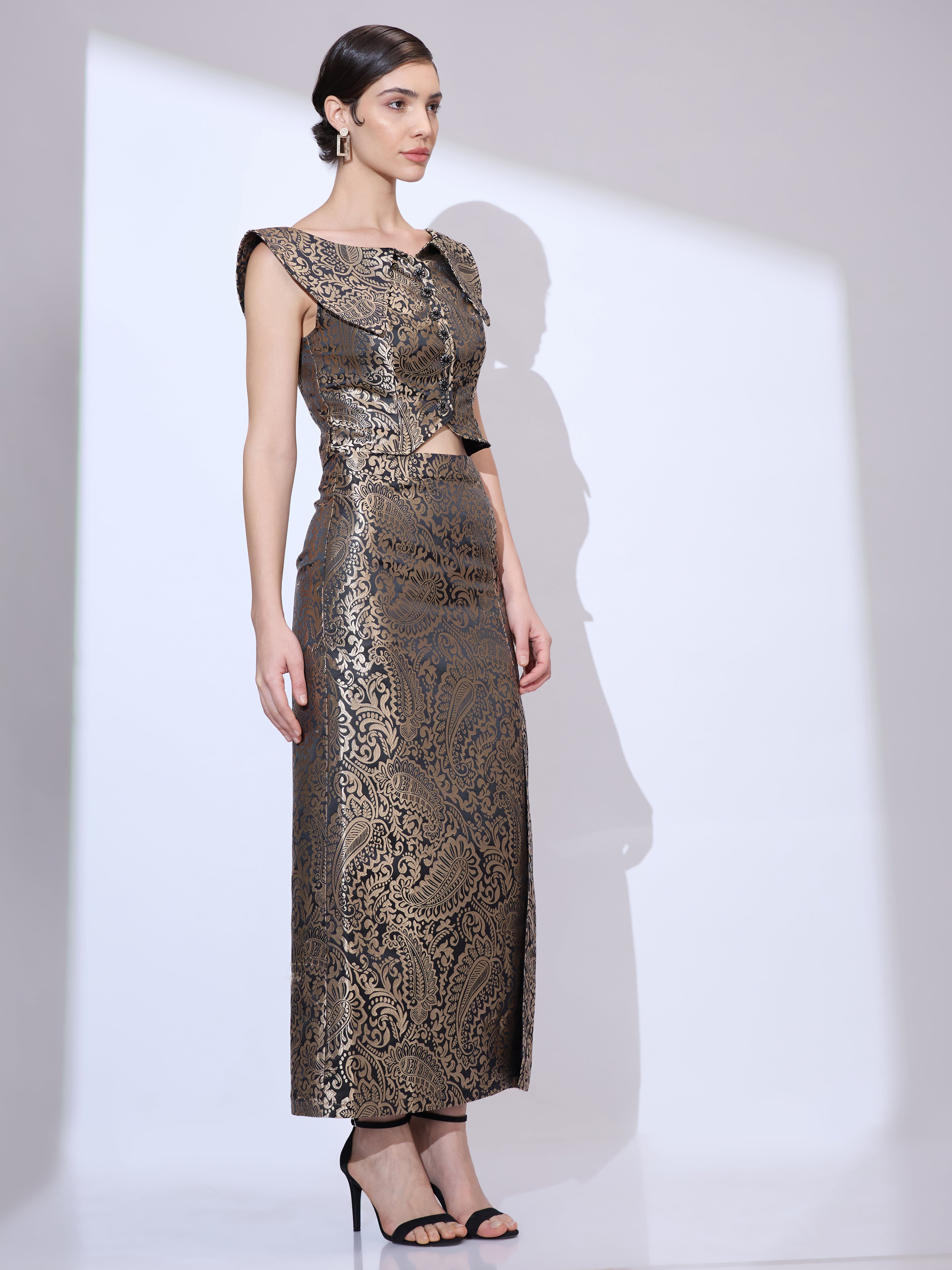 Image of Woman looking to the right wearing a black and gold metallic paisley formal co ord with cropped top and floor-length skirt