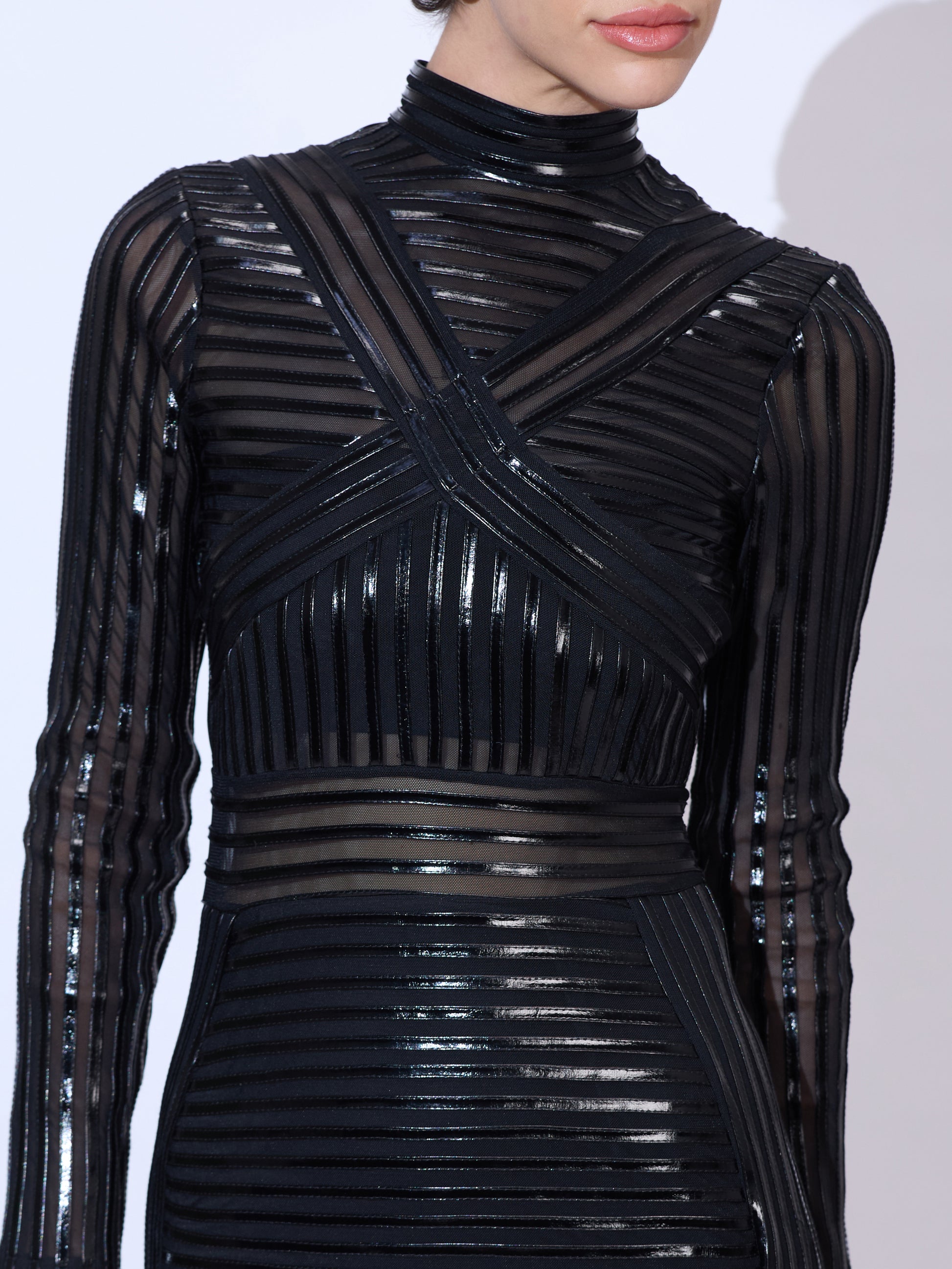 Close-up detail of a black patent vinyl bodycon mini dress with sheer mesh panel accents and mock neck design