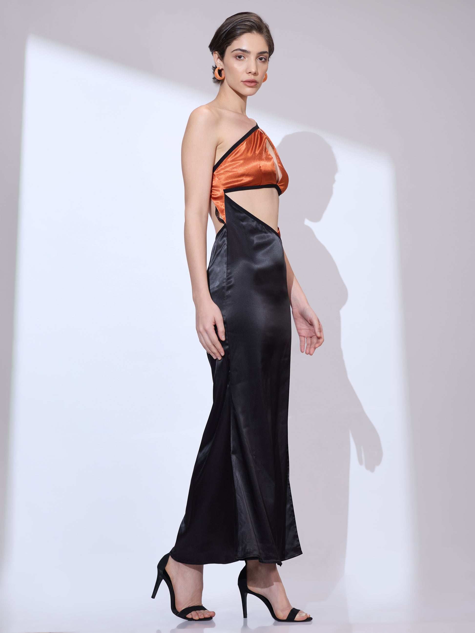 Side view of woman wearing a black silk satin cowl neckline dress with an elegant draped silhouette