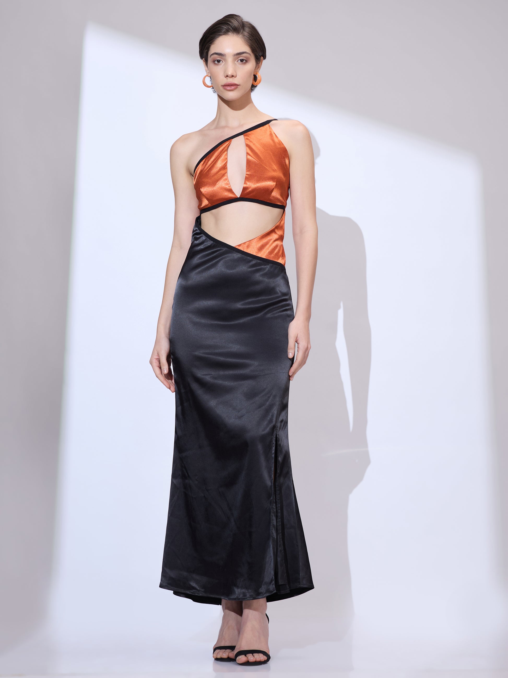 Standing straight in a black silk satin gown with an elegant floor-length silhouette.