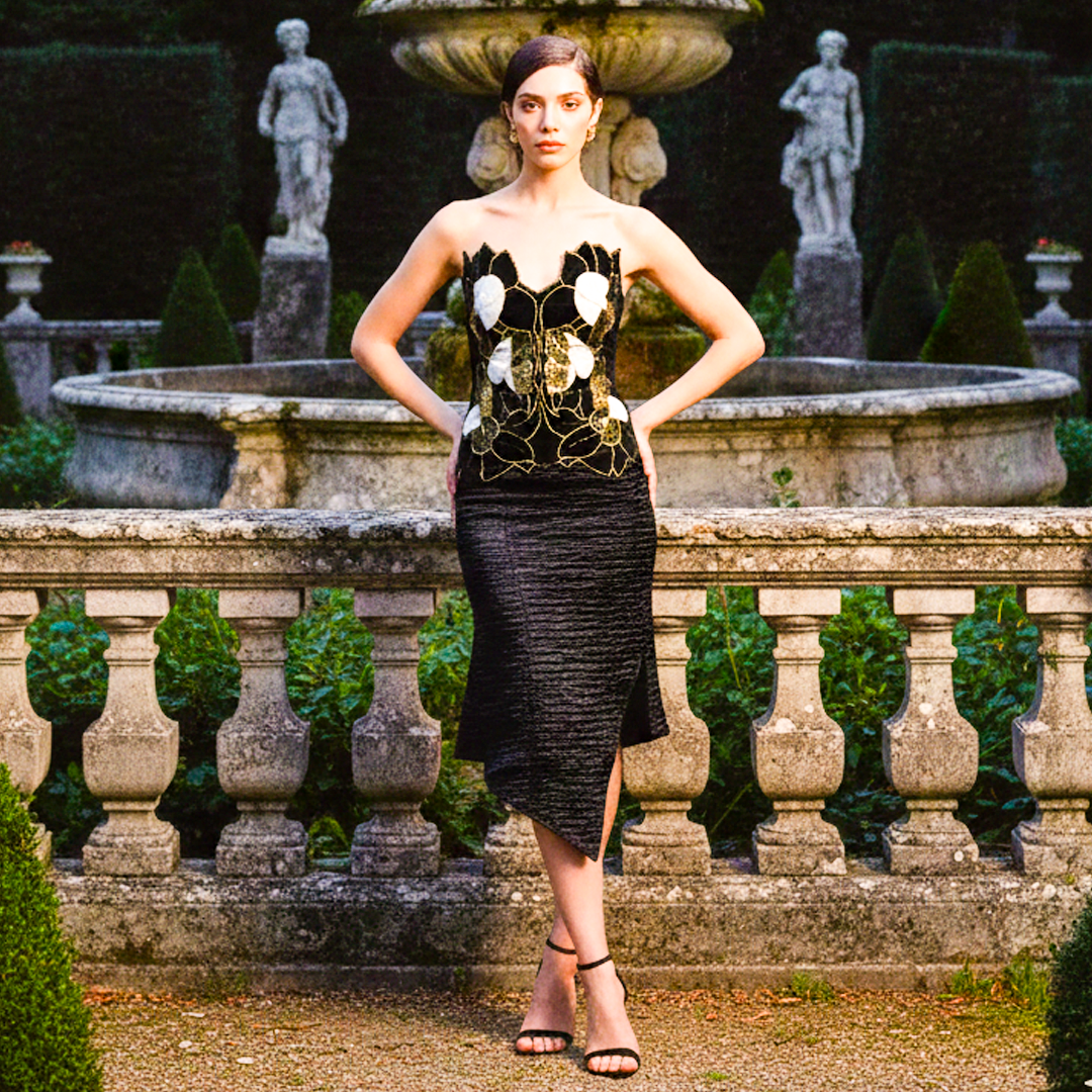Woman facing forward wearing black velvet embroidered strapless midi dress with thigh-high slit.