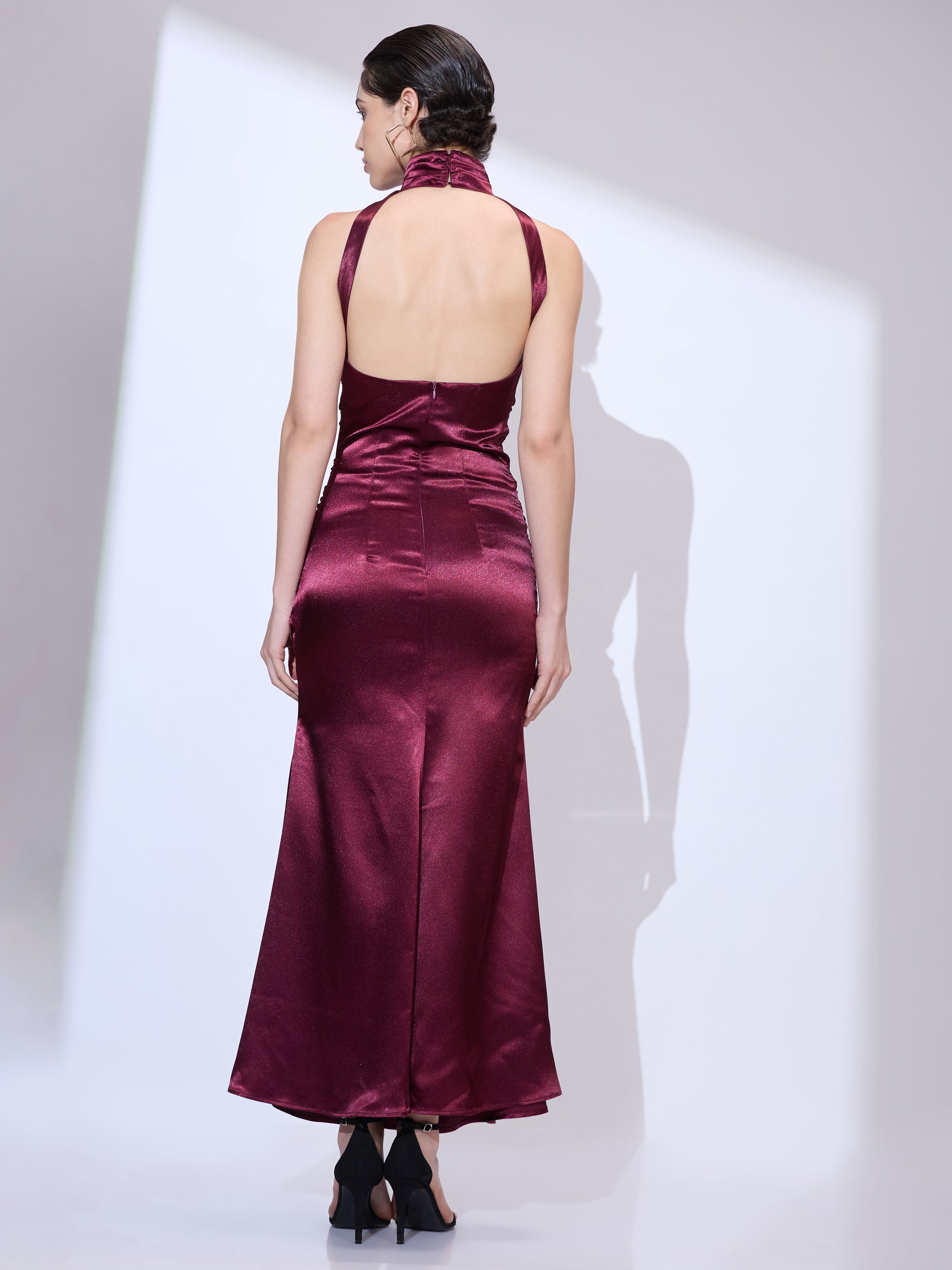 Back view of woman wearing a burgundy silk satin halter maxi dress with elegant floor-length silhouette and ruched detailing
