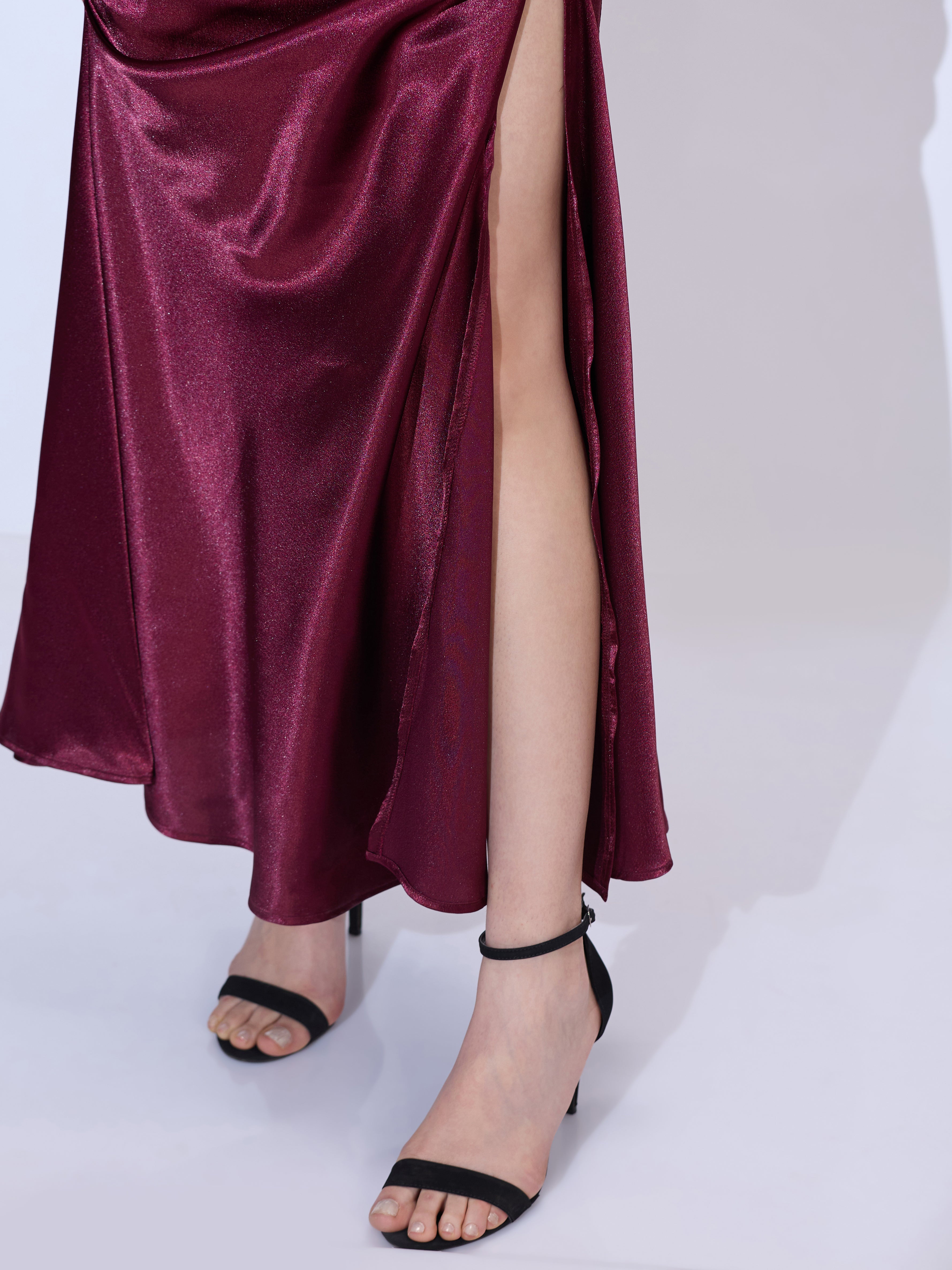 Image of Close-up of the lower silhouette of a burgundy silk satin halter neck maxi dress highlighting the elegant floor-length drape