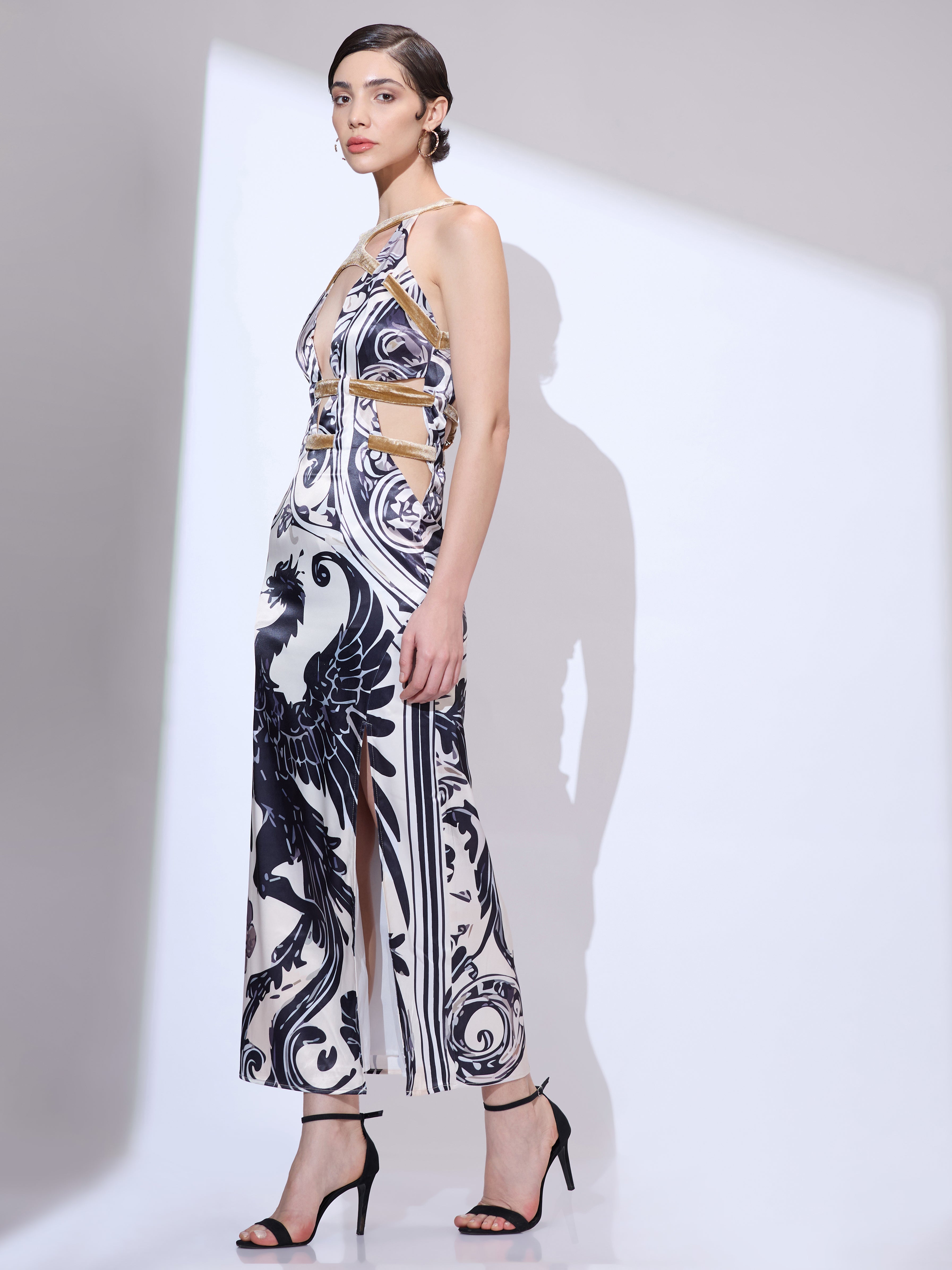 Image of Woman walking left at a side angle wearing a designer maxi gown with black and white dragon print and high side slit