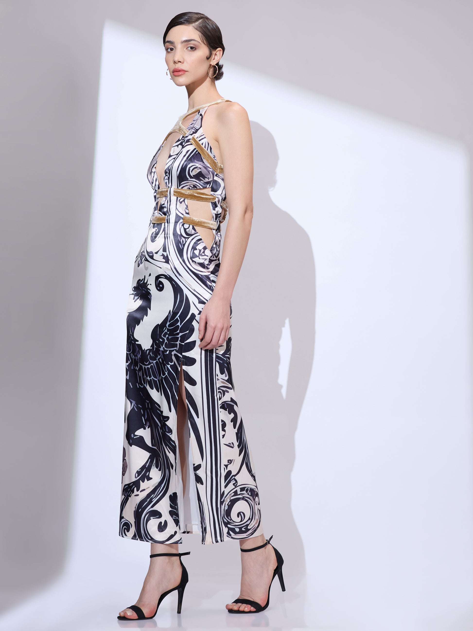 Woman walking left at a side angle wearing a designer maxi gown with black and white dragon print and high side slit
