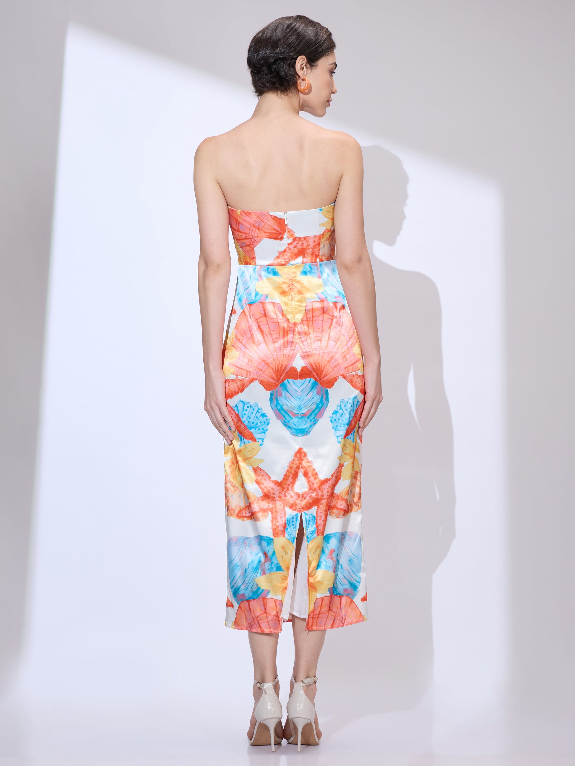 Back view of woman wearing a colorful strapless midi from ladies resort wear with vibrant seashell and starfish print