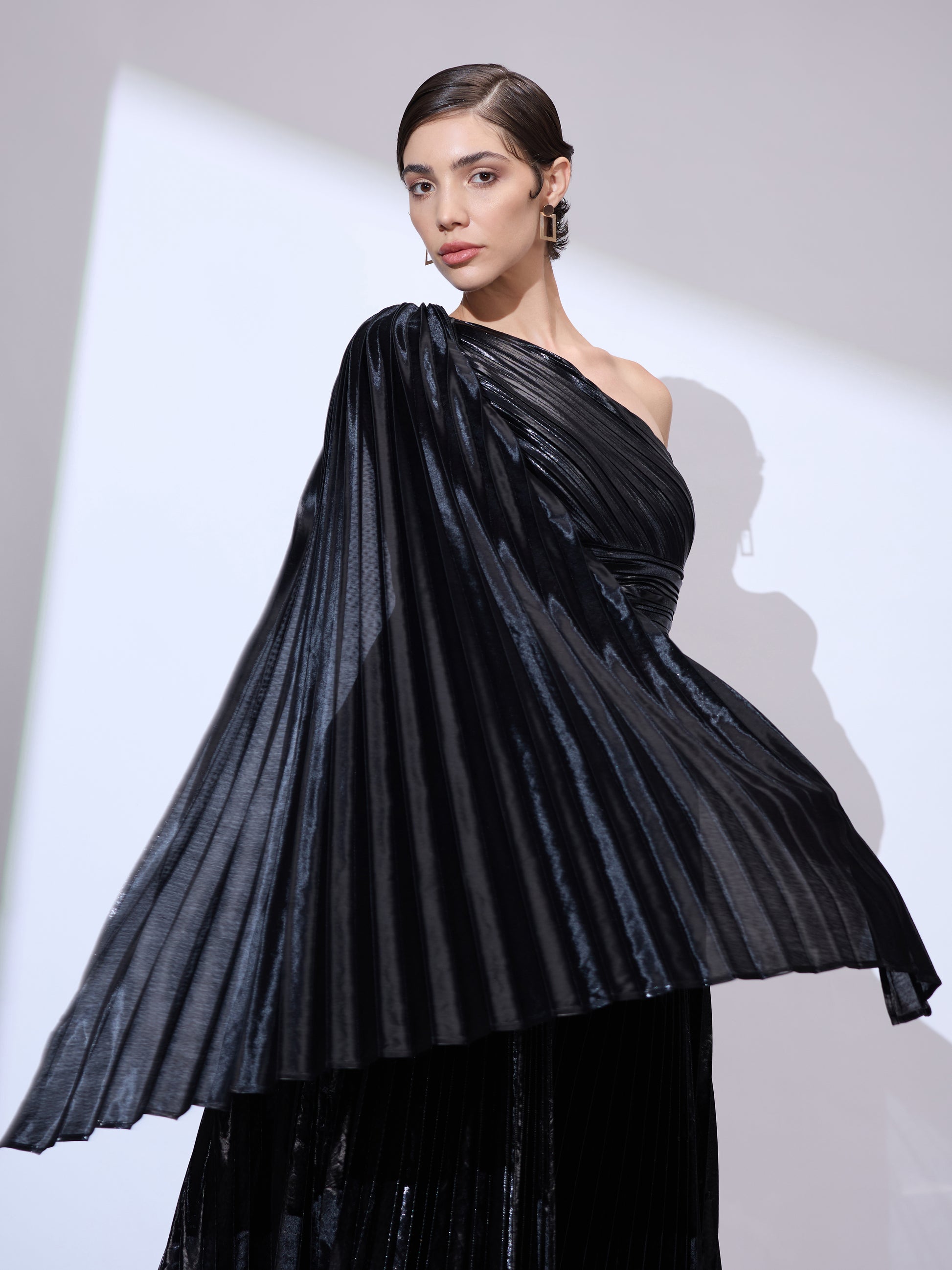 Close-up of woman wearing an asymmetrical neckline gown in metallic pleated fabric with elegant shoulder drape