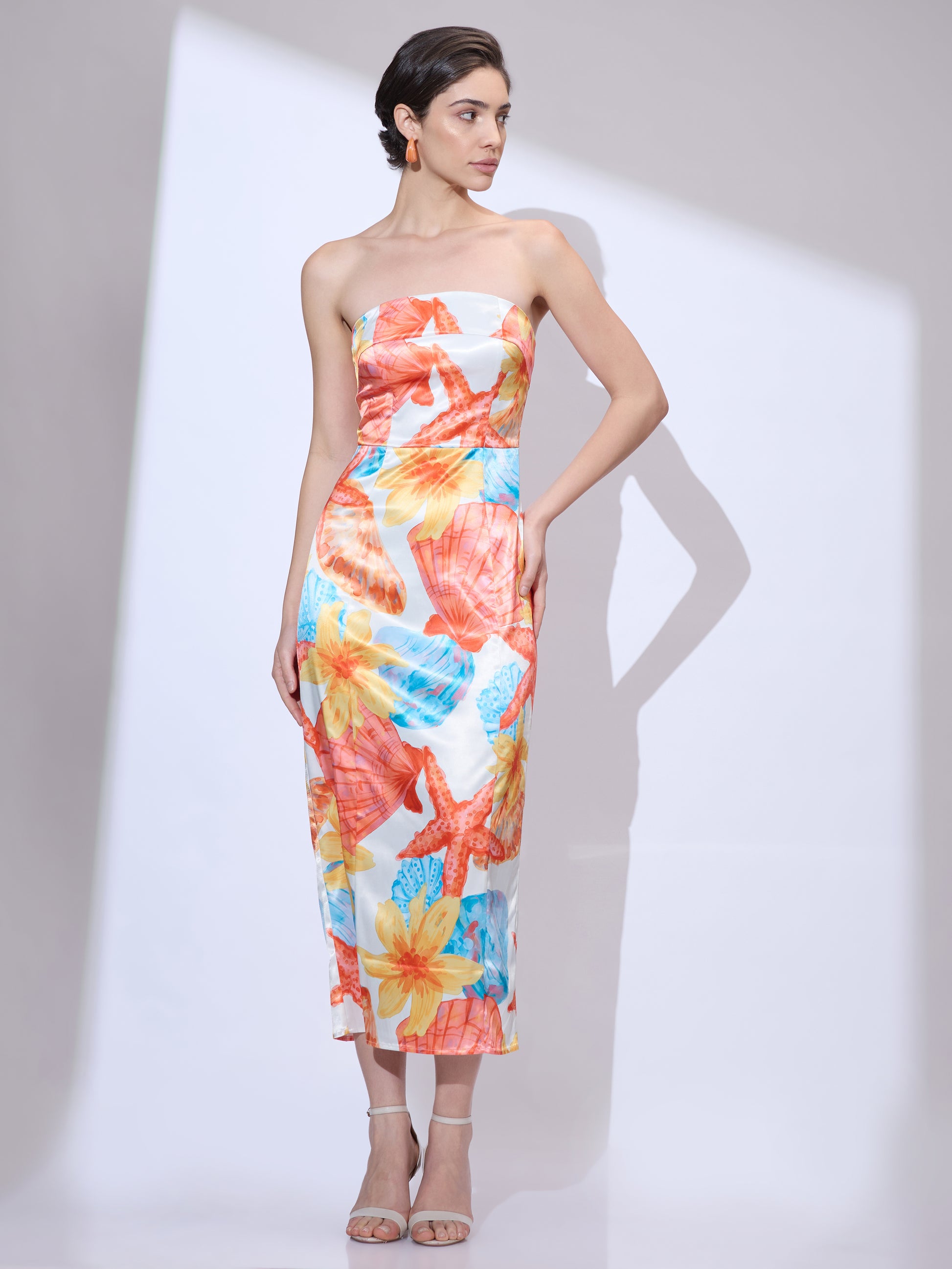 Walking and looking to the side from a side angle in a colorful strapless resort dress featuring seashell and starfish prints