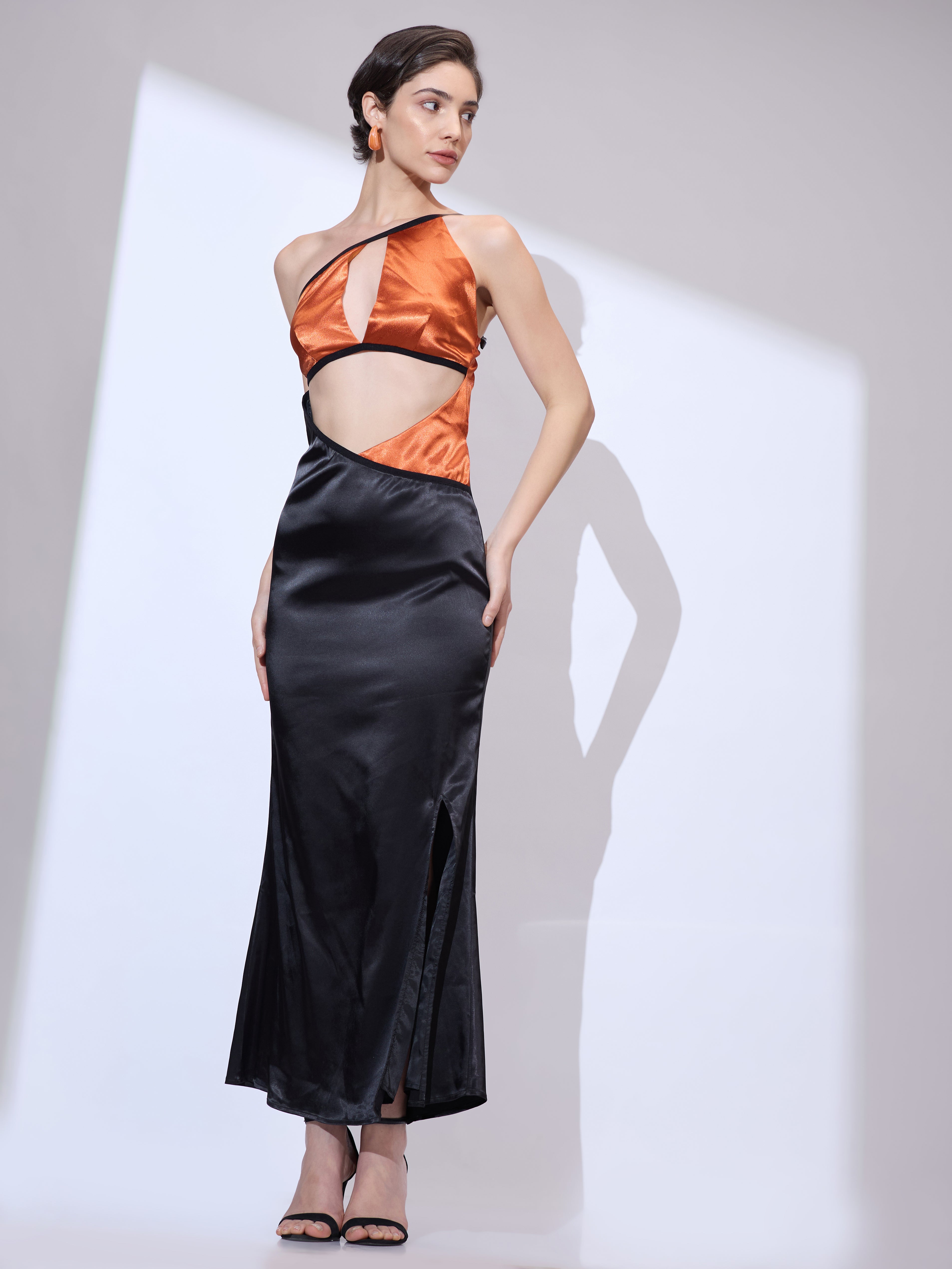 Image of Side glance of woman in a black silk satin maxi gown with a flowing silhouette