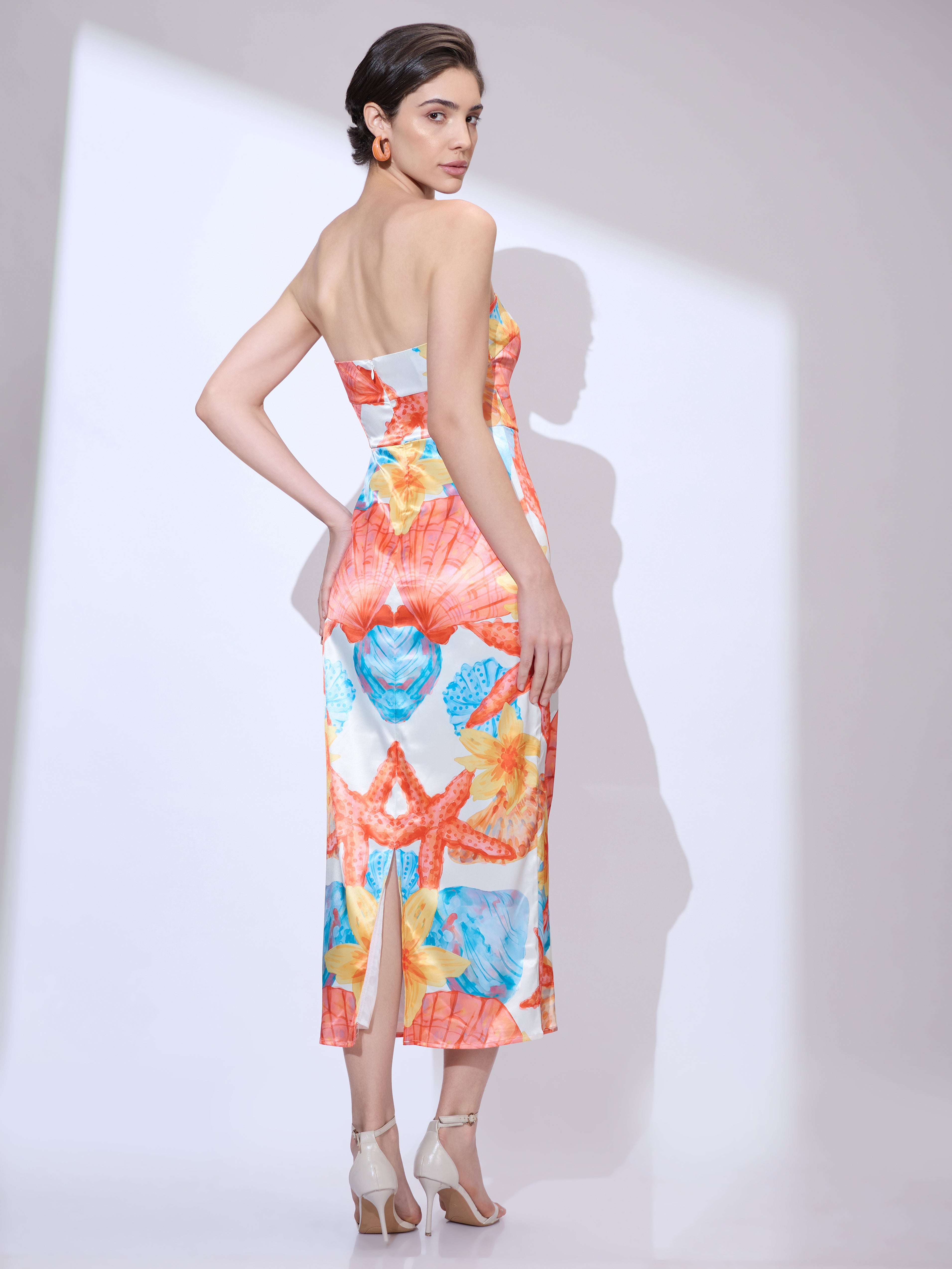 Image of Back view of woman looking over her shoulder wearing a colorful strapless midi dress with vibrant seashell and starfish print