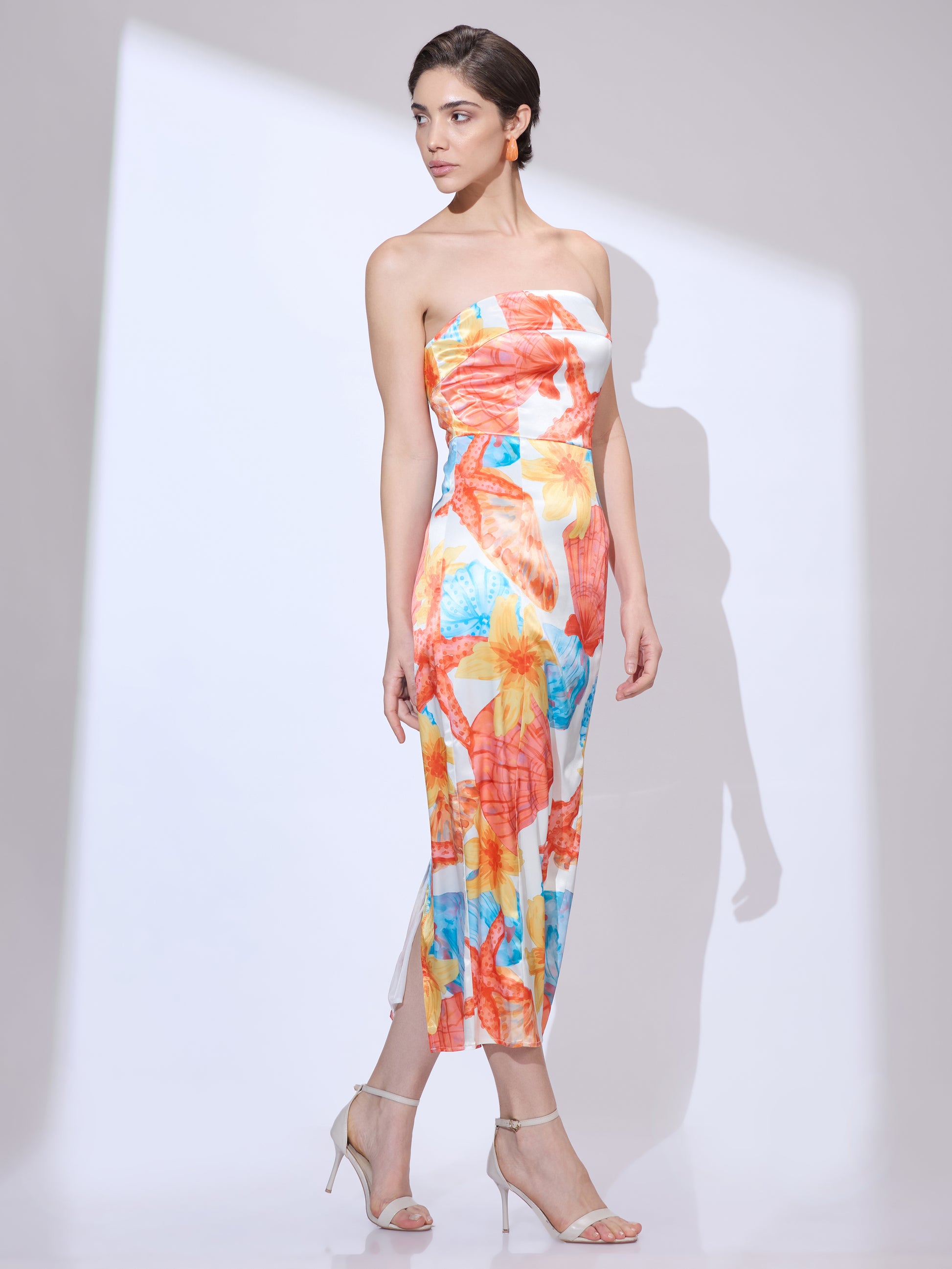 Woman walking and looking side from a side angle wearing a colorful strapless resort dress with seashell and starfish print